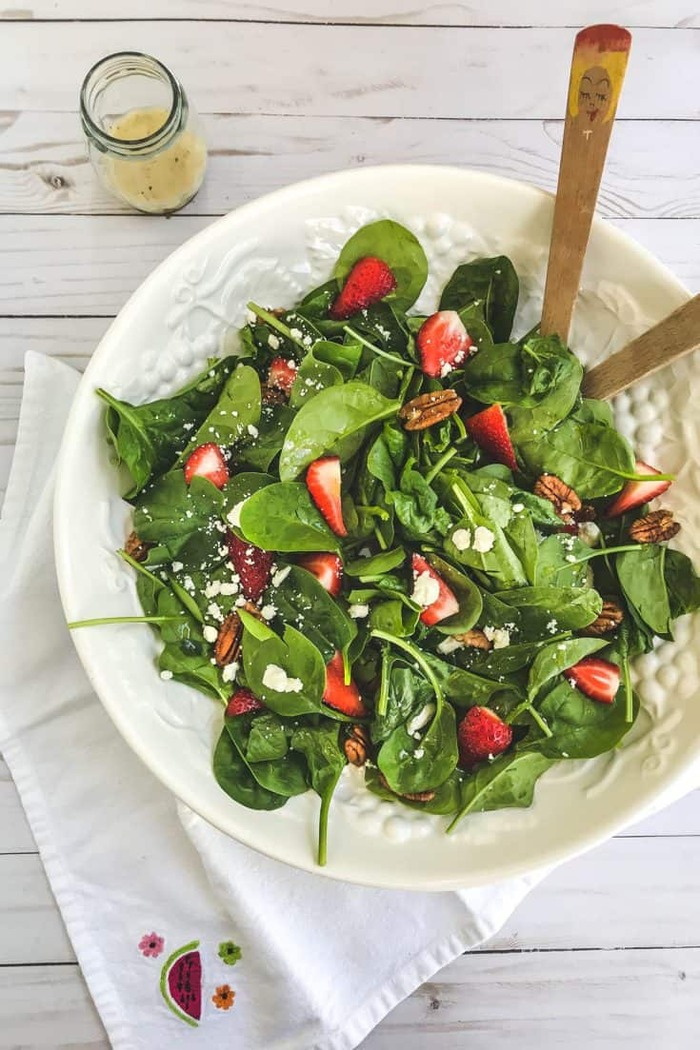 spinach salad healthy easter menu green spinach salad on a white table in a large white bowl with dressing in a jar on the side