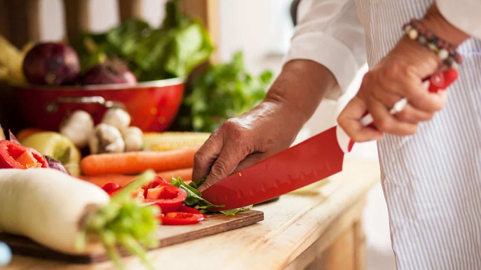 vegan easter menu woman in a white kitchen cloth cutting vegetable with a large red knife on a wooden surface