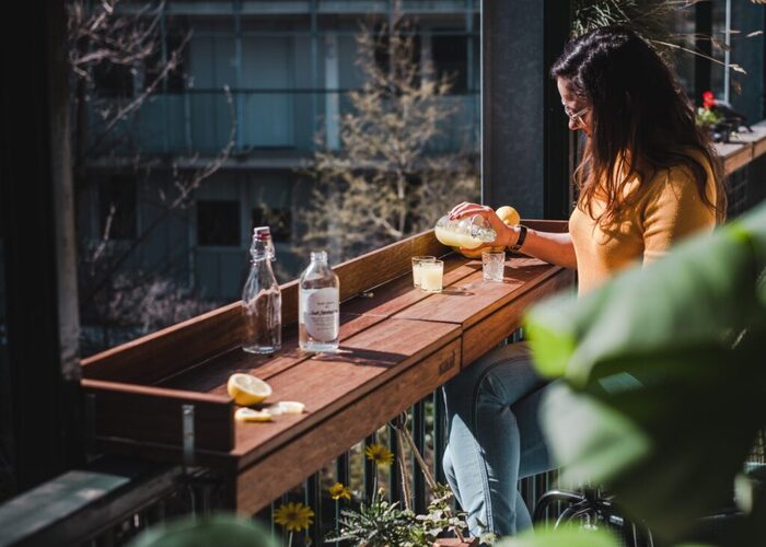 woman with dark hair and glasses standing at a wooden balcony bar pouring drinks