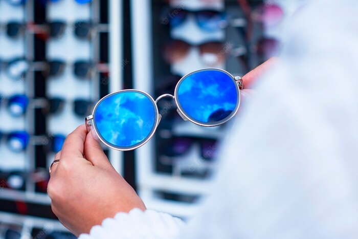 woman in white holding a pair of blue sunglasses