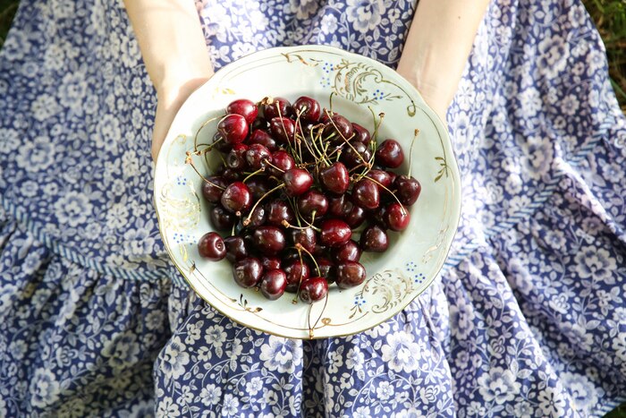 woman in a vintage blue and white dress holding a plate of cherries