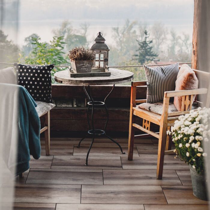 cute balcony with a small table and two wooden chairs with decorative cushions and throws