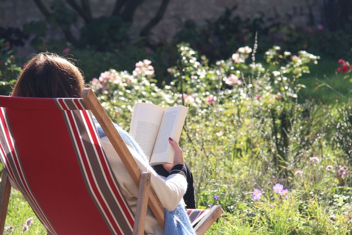 woman sitting in the sun in a chair in a picture perfect garden reading a book