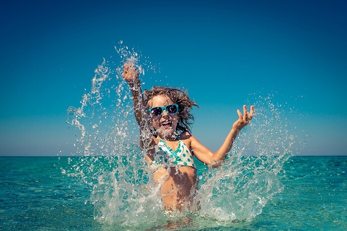 little girl in swimming suit with blue sunglasses on enjoying the sea water and splashing around