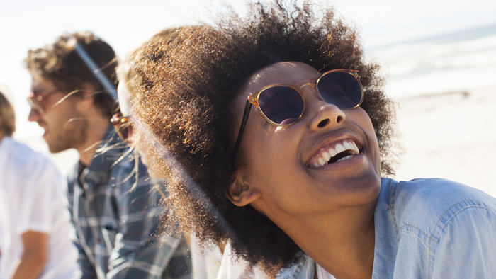 Smiling friends at beach woman with afro hair and sunglasses looking at the sun smiling