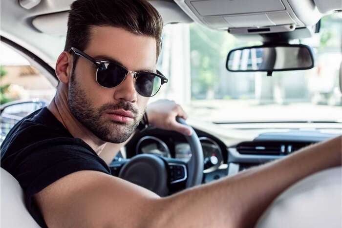 man dressed in a black short sleeve shirt in a car wearing a pair of dark sunglasses