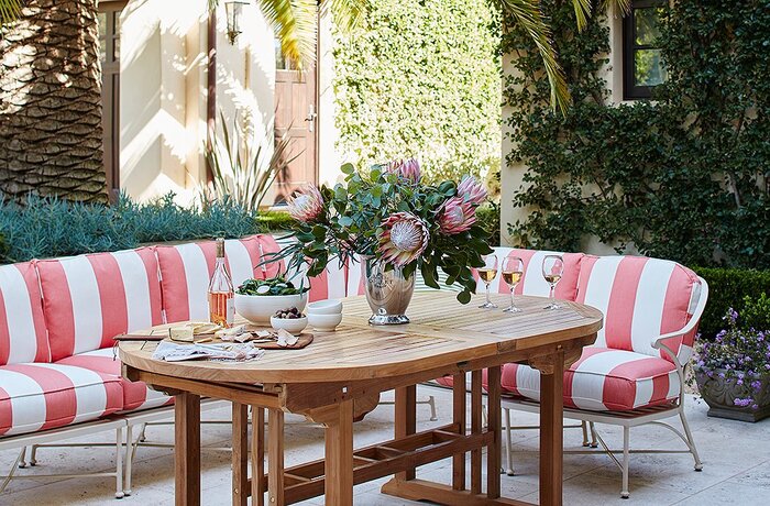 outdoor dining area with a wooden table and white and pink striped chairs with greenery all around