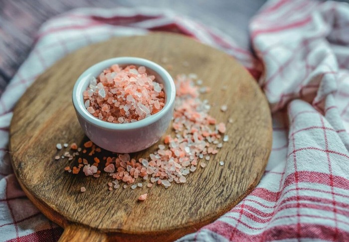 pink salt crystals in a white bowl on a wooden surface placed on a white and red table cloth