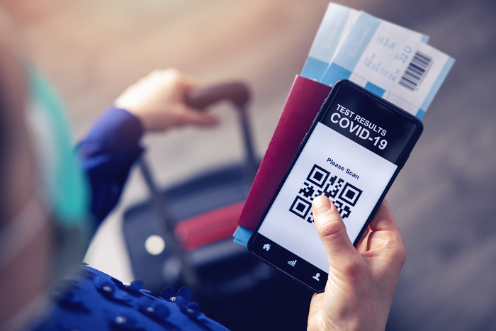 Person with a mask holding their passport tickets and phone with their covid results and a suitcase