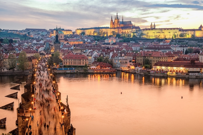 prague and charles bridge at sunset with people walking on the bridge over the river