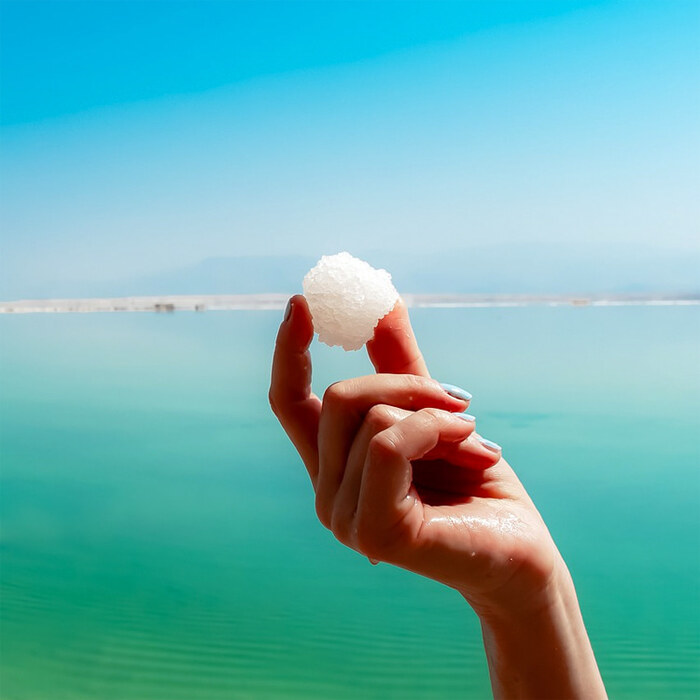 woman's hand holding a piece of salt with blue water in the background
