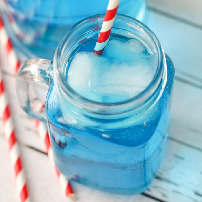 bright blue salty water in a glass jar with ice cubes in it and red and white straw on a white wooden table