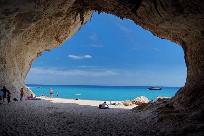 sardinia cala luna beach viewed from a cave with people sunbathing and a clear sky 