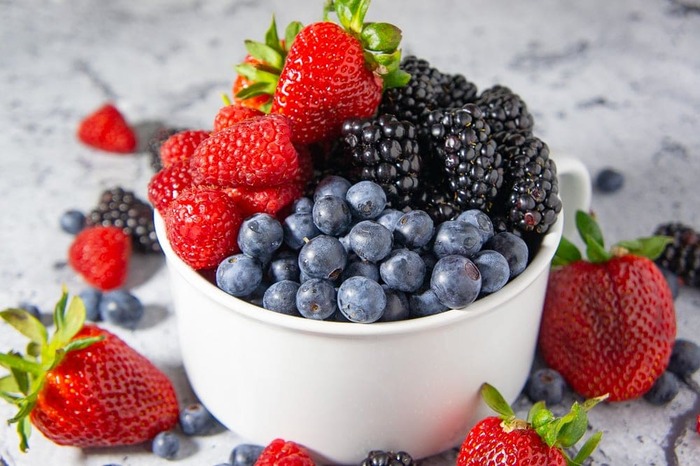 a white bowl full of fresh summer berries strawberries blue berries and more