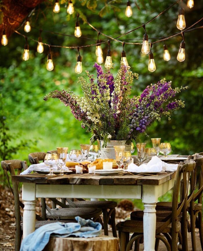 beautifully decorated outdoor wooden table with tall flower arrangement centerpiece and string lights