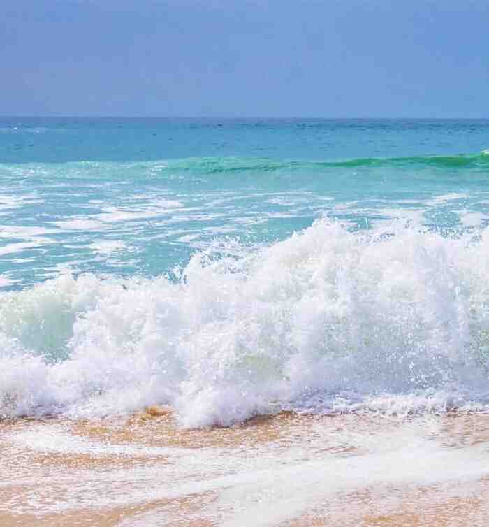 sandy beach and sea waves with white foam and blue sky in the background