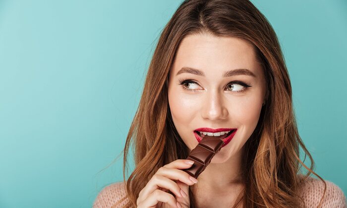 woman looking aside on a blue background eating chocolate