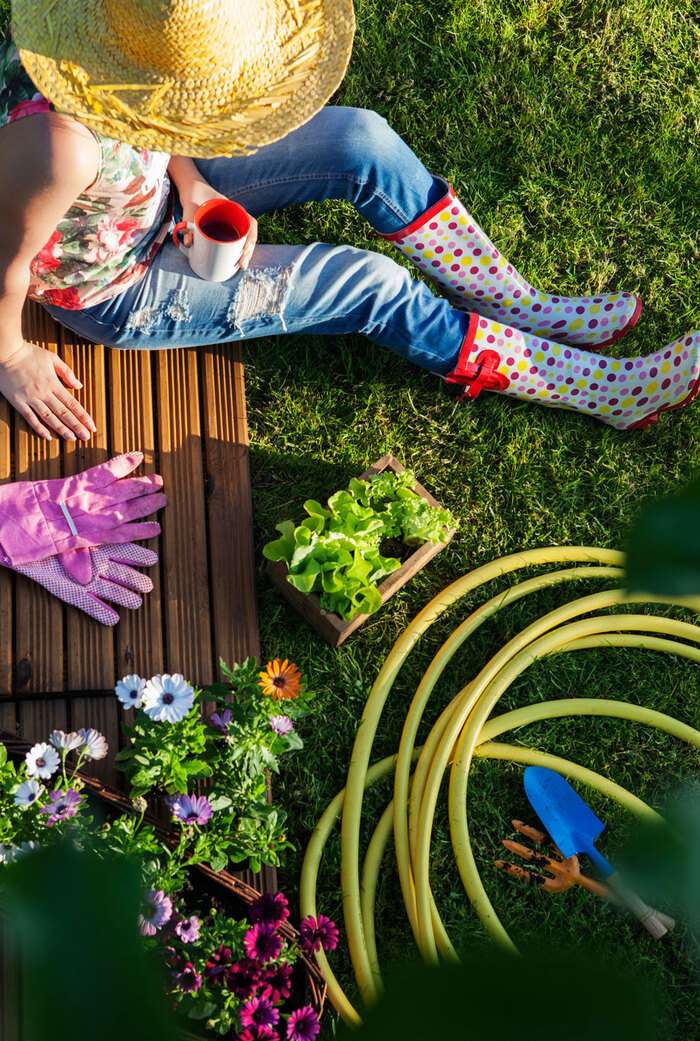 woman with a sunhat sitting outside in the grass with pink gardening gloves and rubber boots on