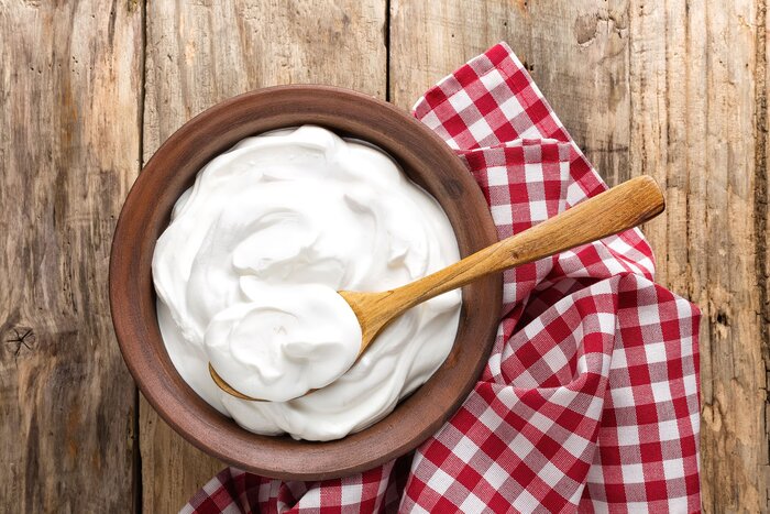 a brown bowl full of fresh plain yoghurt on a red and white checkered kitchen towel with a wooden spoon