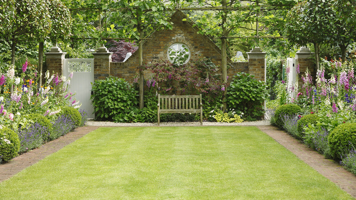 English garden with an open space short green grass flower borders and a bench 