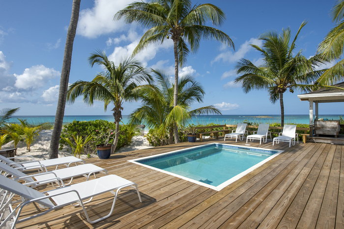 bahamas villa with an outdoor pool and white poolside chairs and tall palm trees