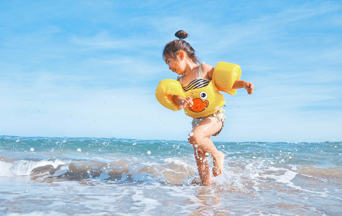 beach safety for kids little girl in her swimsuit and yellow beach gear smiling and jumping into the water