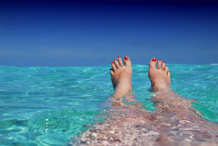 woman's legs in clear water with red nailpolish showing on the surface
