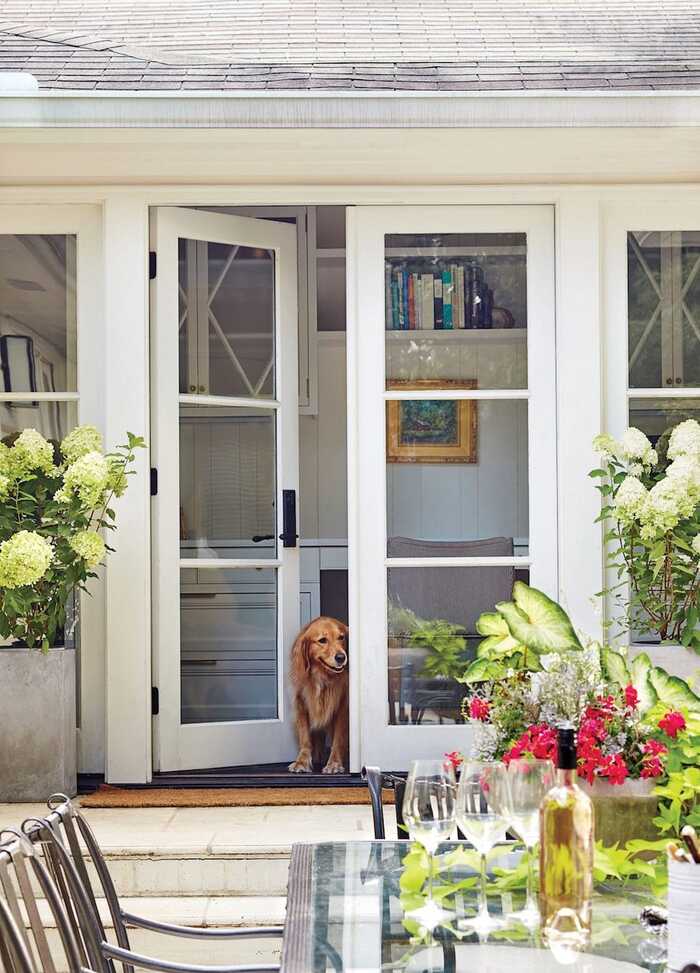 exterior white french patio doors to a nice garden with an arranged table and a dog looking outside from the open doors