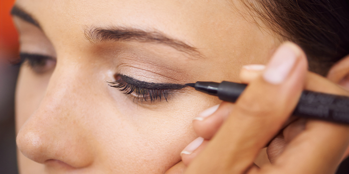 close up on a woman's eyes and a make up artist applying eyeliner to her eye
