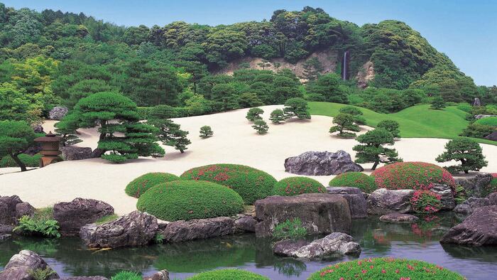 japanese garden large open space with yellow sand and green bushes next to a creek