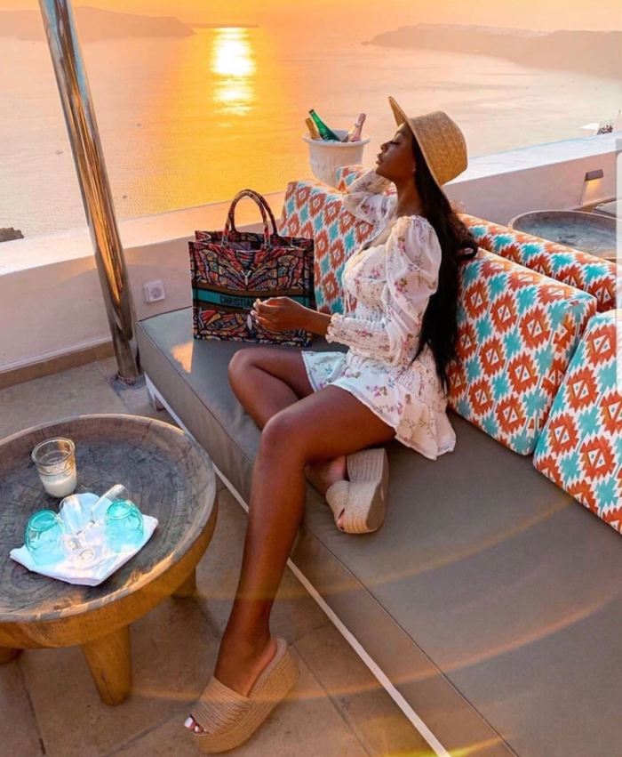 woman in short white dress enjoying a luxury vacation relaxing at a beach bar overlooking the sea and the sunset