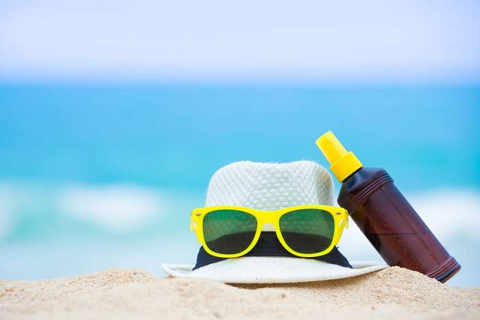 protect your skin from the sun a sun hat with yellow and green sunglasses and a bottle of sun protection spray