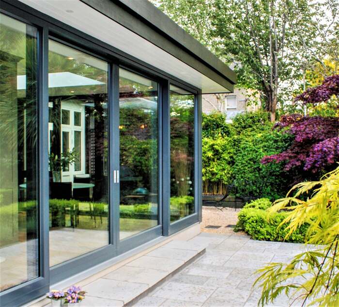 dark sliding patio doors looking to a green garden with trees and bushes and a tile covered patio