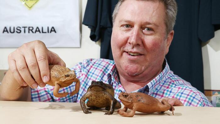 Man looking at the camera showing three stuffed toads in front of him 