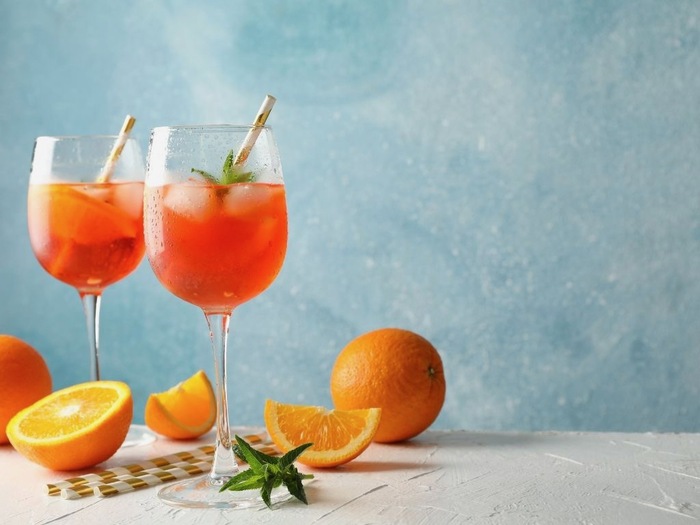 Aperol spritz in elegant glasses on a light blue background with slices of orange scattered around