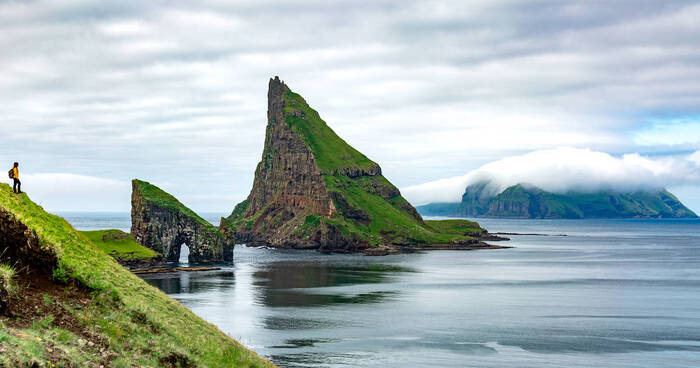 faroe islands sea and green rocks with a woman standing on a cliff overlooking the scenery