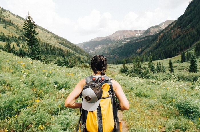 hiking trip woman with yellow backpack walking through a green meadow 