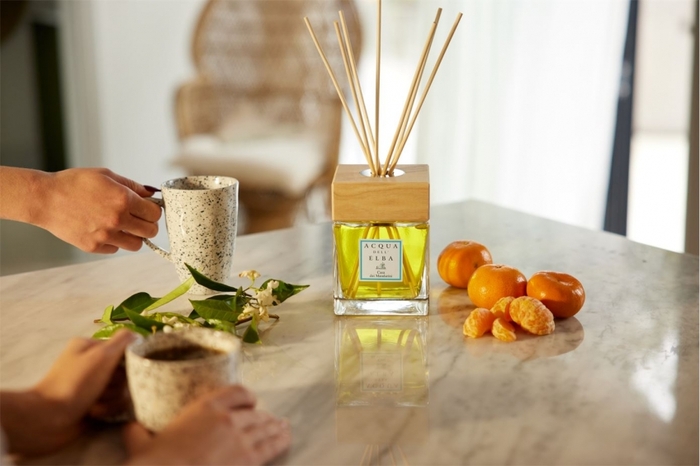 home scent home perfume on a table with tangerines and two people with mugs in their hands 