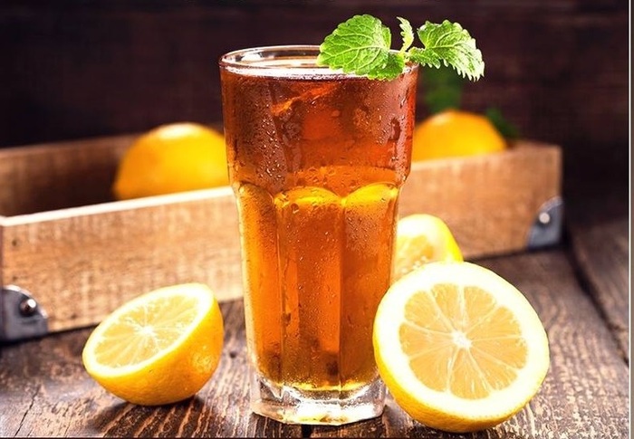 large glass of ice tea on a wooden surface with two pieces of lemon on the site and a bit of mint on top