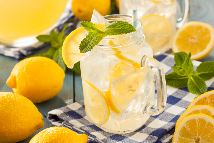 Homemade refreshing yellow lemonade with ice and mint surrounded by whole lemons 