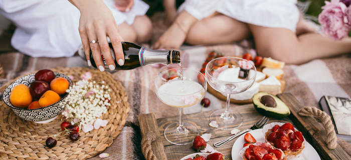 romantic picnic two women sitting in the background one is pouring sparkling wine into elegant glasses