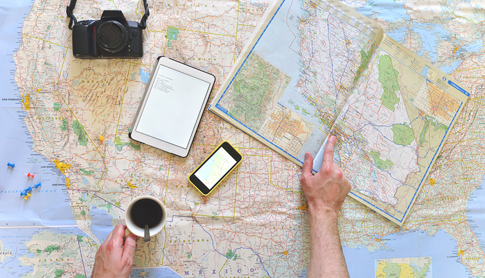 planning a roadtrip mans hands on a table covered with maps holding a coffee with his photo camera phone and tablet on display