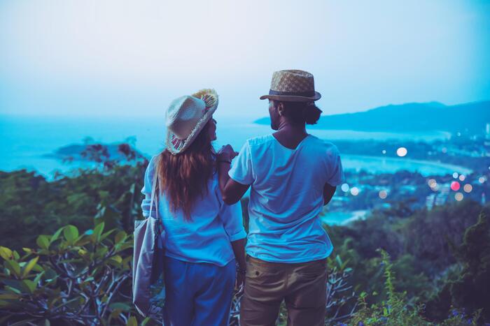 romantic picture of a couple overlooking the sea from a high spot surrounded by Nature and trees