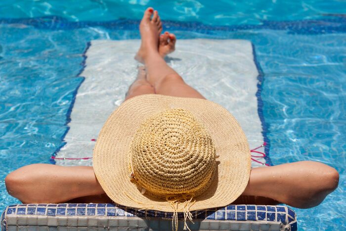 woman laying in the sun with her body in a pool with her sun hat on and her back to the camera