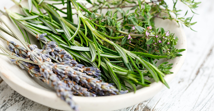 trimmed herbs in a white bowl on a white wooden table rosemary lavender and thyme