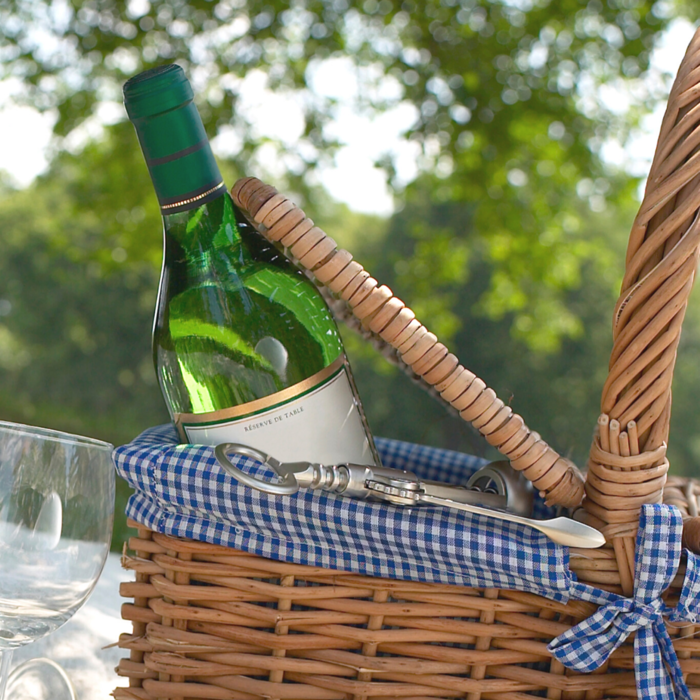 vintage picnic basket outside with a bottle of wine sticking from it 