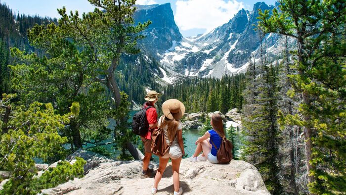 visit natural parks three people with summer hats sitting on a rock enjoying the view over snowy mountains and forests