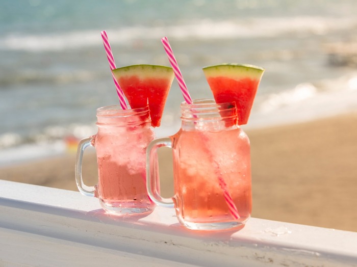 watermelon lemonade in mason jars on a beach decorated with slices of watermelon and red and white straws