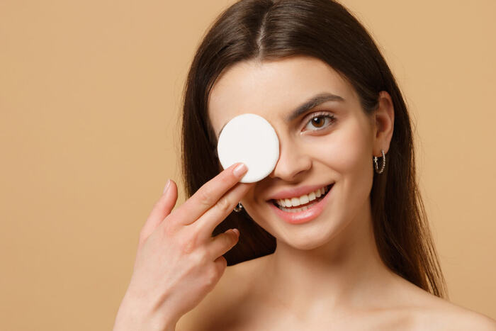 waterproof make up woman with long hair looking and smiling at the camera holding a cotton pad on her eye