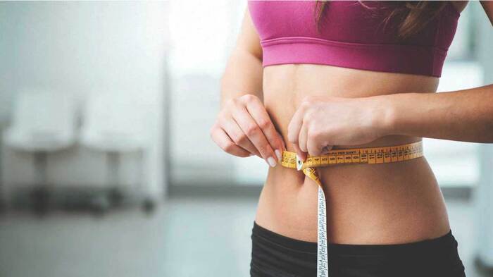 wight loss woman in sportswear measuring her waist with a yellow measuring tape